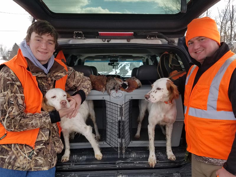 Two dogs and their owners standing next to an Easy Loader Kennel after a successful hunt